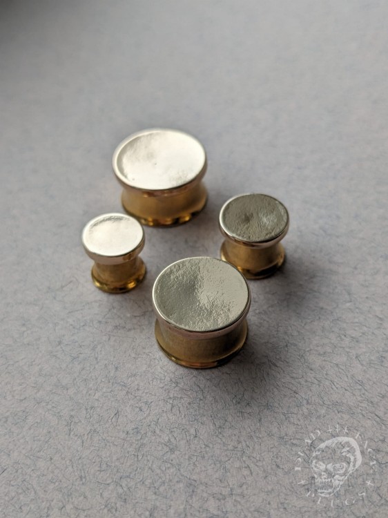 Mirror finished bronze disc plugs looking like solid gold gauges on stainless steel tunnels
