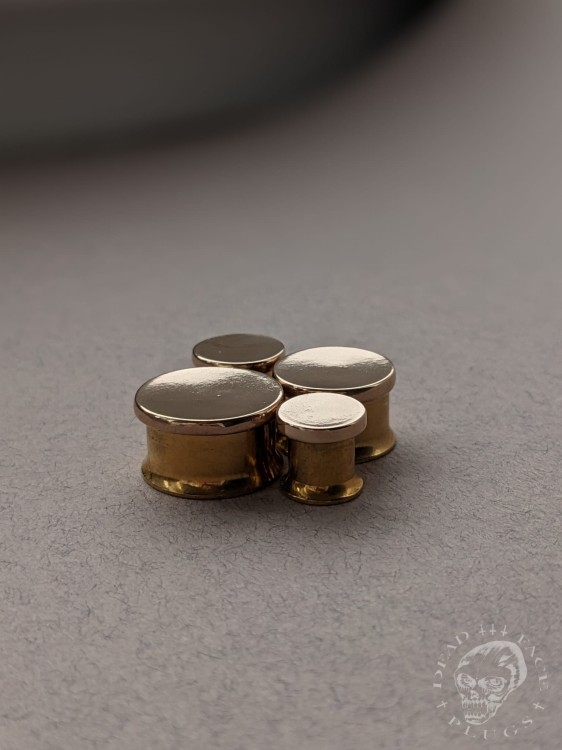 Mirror finished bronze disc plugs looking like solid gold gauges on stainless steel tunnels