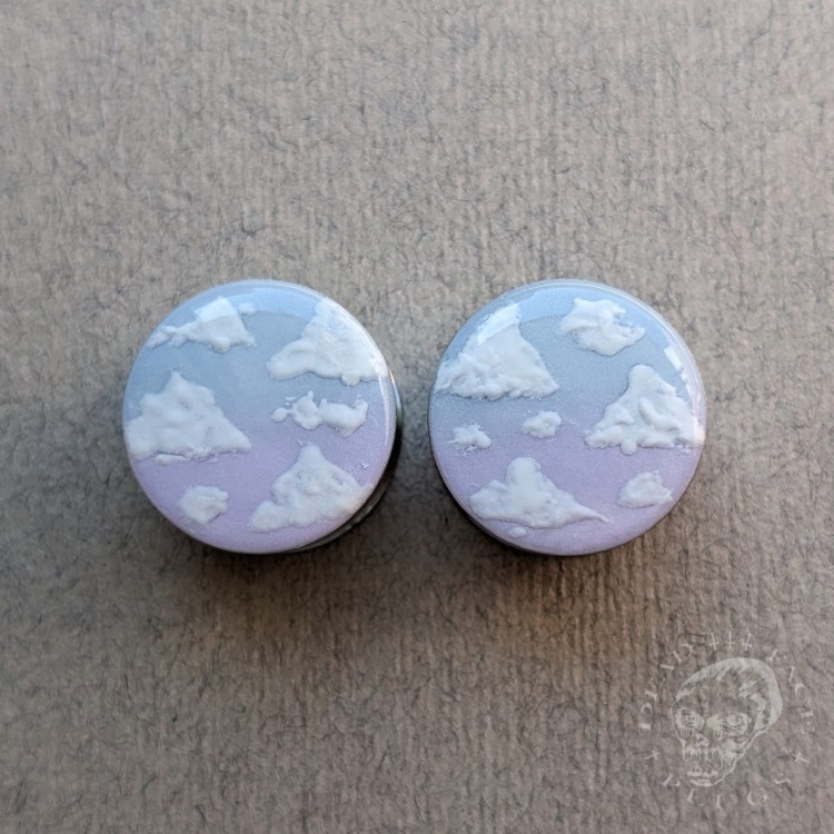 Silver ear plugs with blue and lilac violet purple ombre effect, decorated with fluffy white clouds.