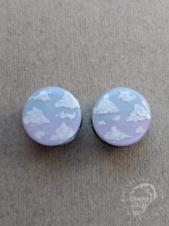 Silver ear plugs with blue and lilac violet purple ombre effect, decorated with fluffy white clouds.