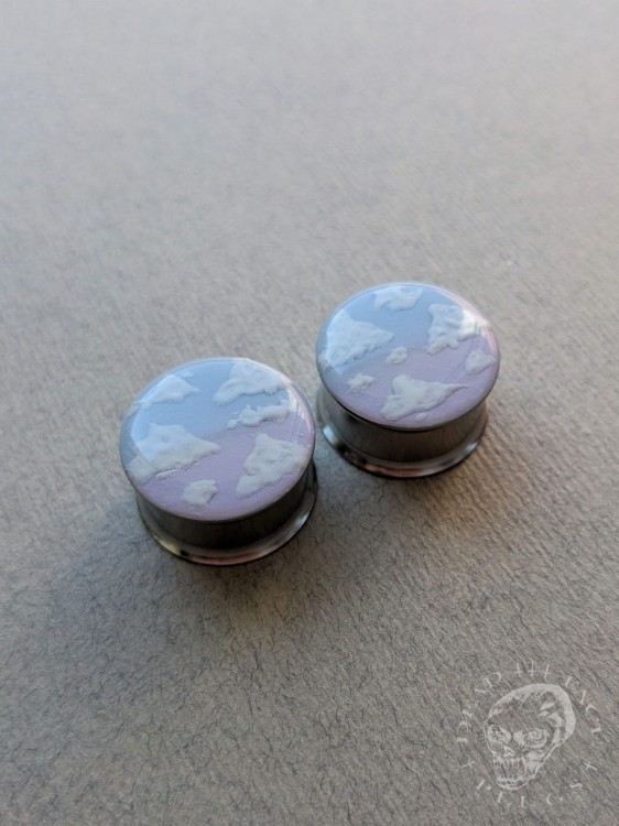 Silver ear plugs with blue and lilac violet purple ombre effect, decorated with fluffy white clouds.