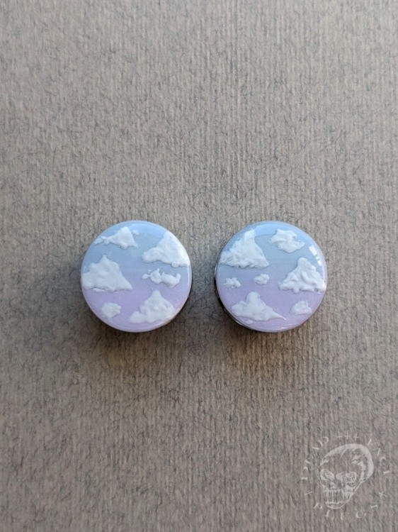 Silver ear plugs with blue and lilac violet purple ombre effect, decorated with fluffy white clouds.