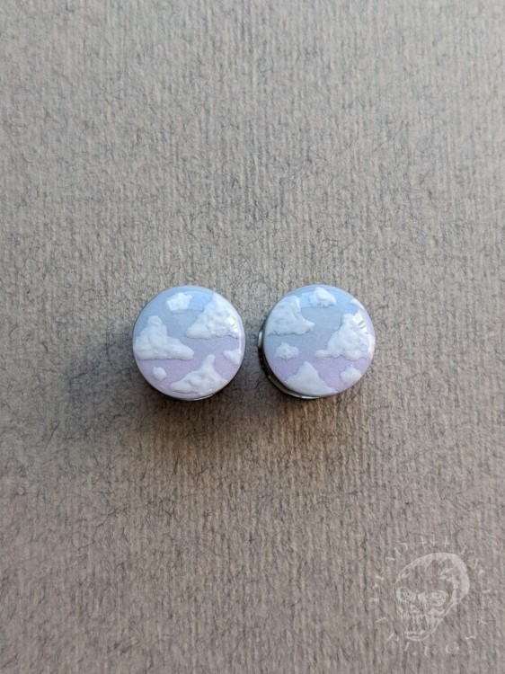 Silver ear plugs with blue and lilac violet purple ombre effect, decorated with fluffy white clouds.