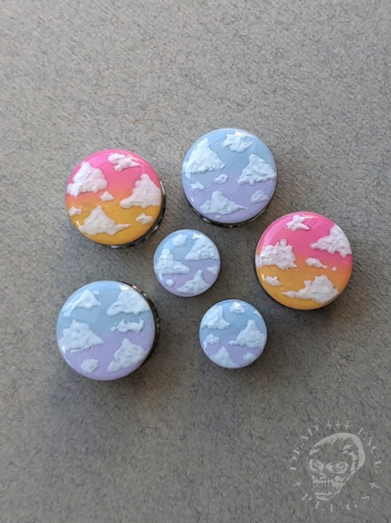 Silver ear plugs with blue and lilac violet purple ombre effect, decorated with fluffy white clouds.
