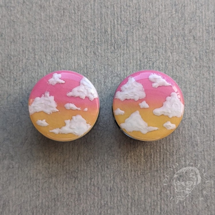 Silver ear plugs with pink and yellow ombre effect, decorated with fluffy white clouds.