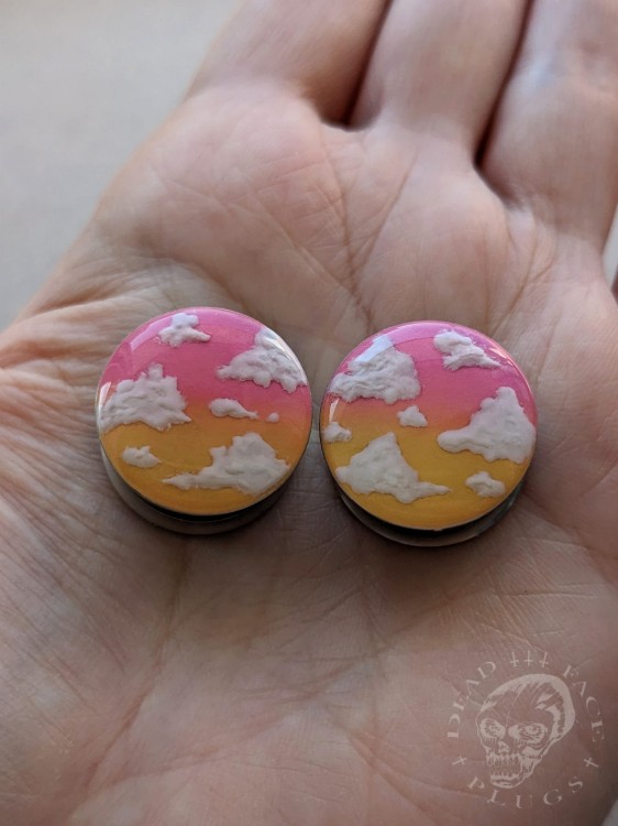 Unique ear plugs on silver tunnels with ombre colors and fluffy white clouds.