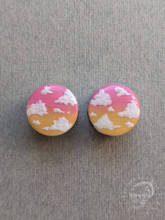 Unique ear plugs on silver tunnels with ombre colors and fluffy white clouds.