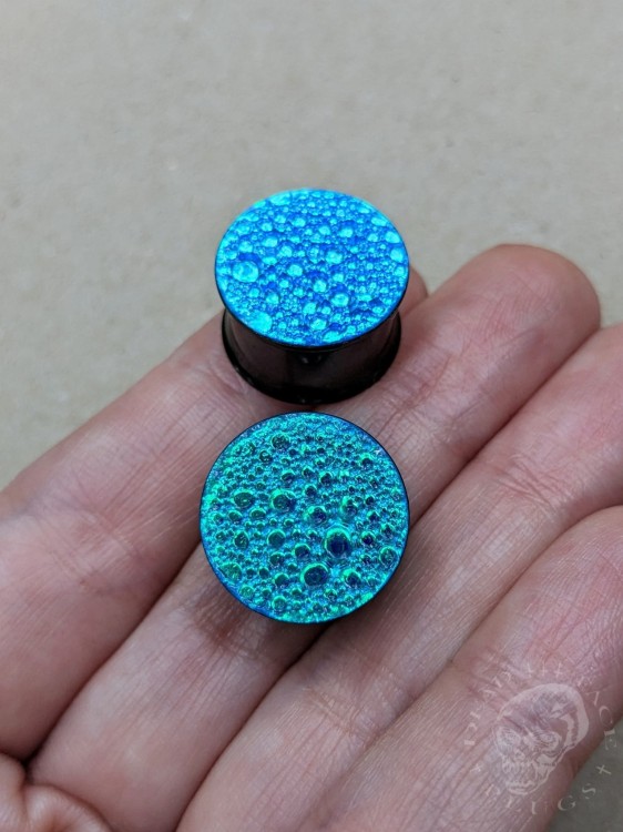 Black steel ear plugs with color-shifting effect in sapphire blue and emerald green, textured finish
