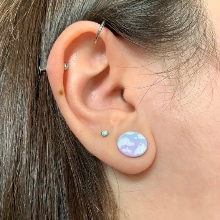 Silver ear plugs with blue and lilac violet purple ombre effect, decorated with fluffy white clouds.